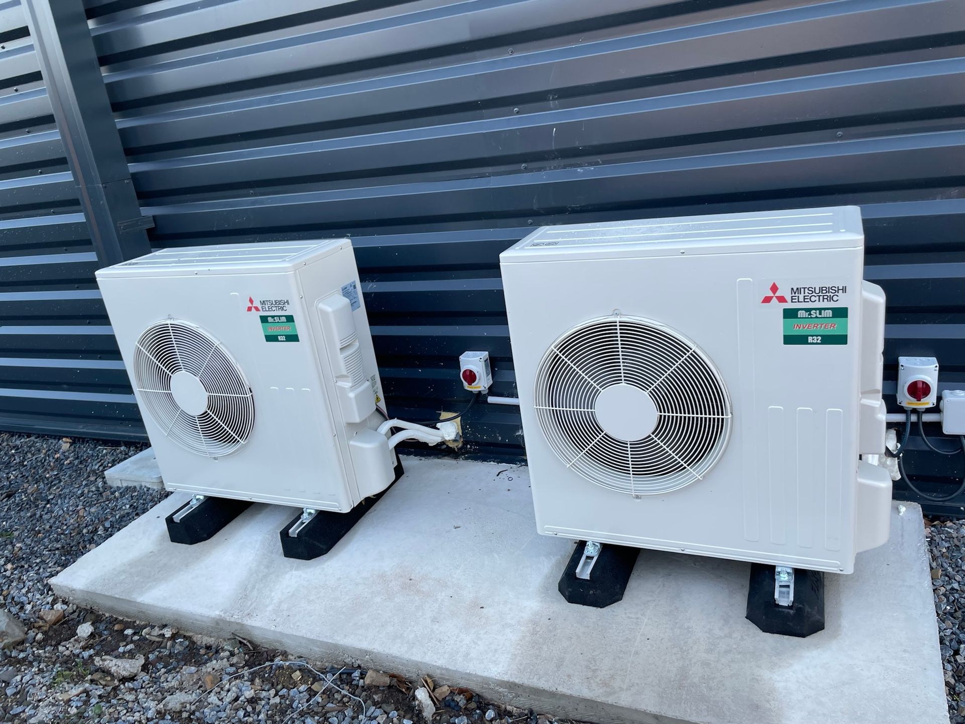 Deux unités de climatisation blanches sur une dalle de béton contre un bâtiment.