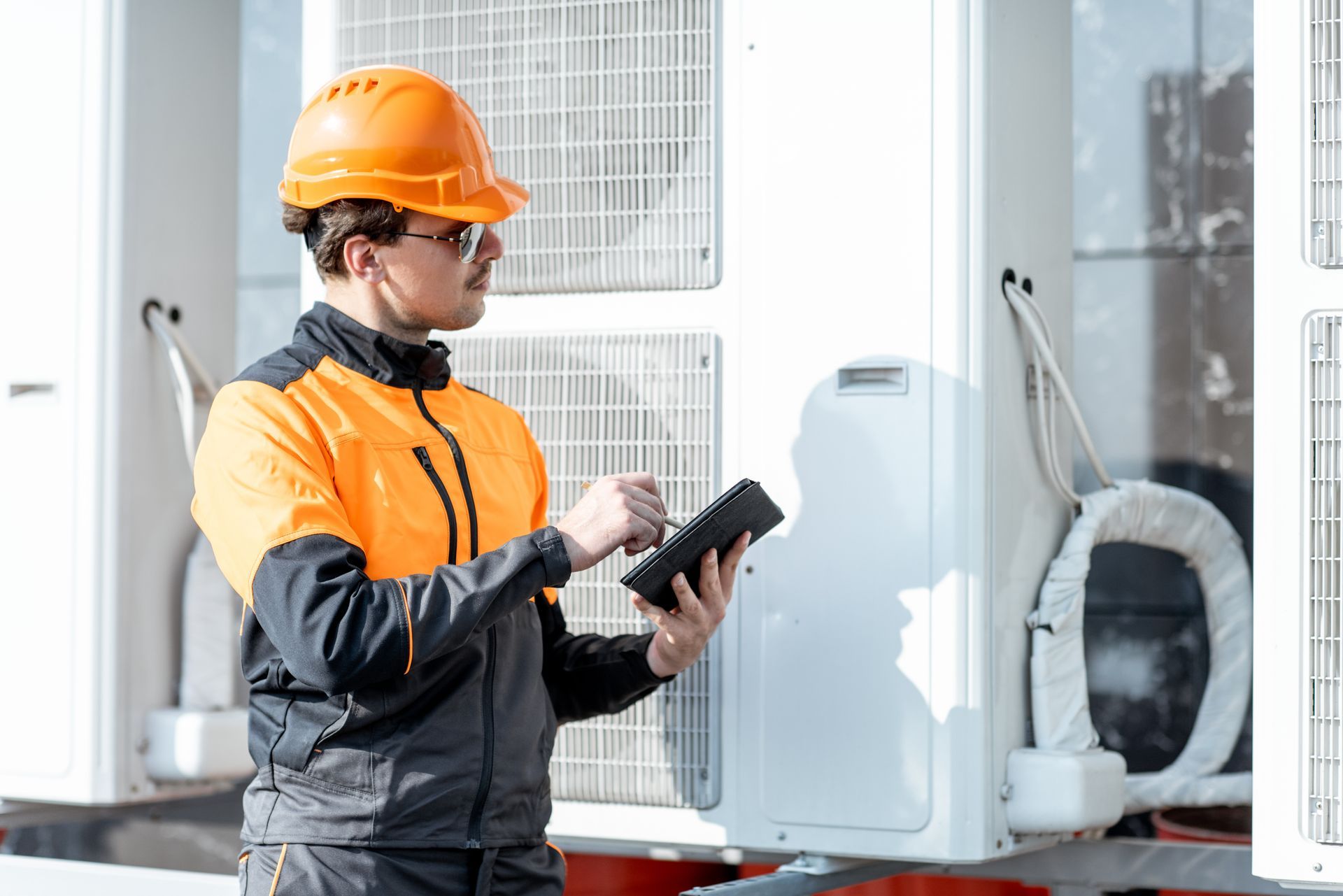 Ouvrier portant un casque orange utilisant une tablette à côté d'un équipement de pompe à chaleur