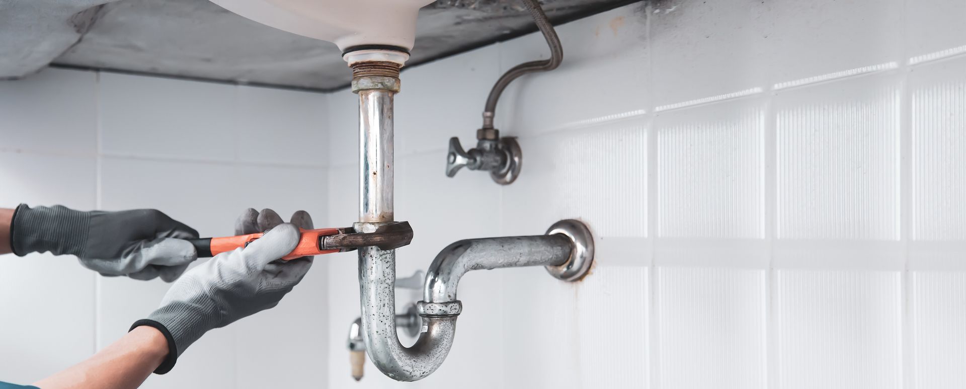 Quelqu'un tient une clé à molette qui dévisse un tuyau métallique sous un lavabo