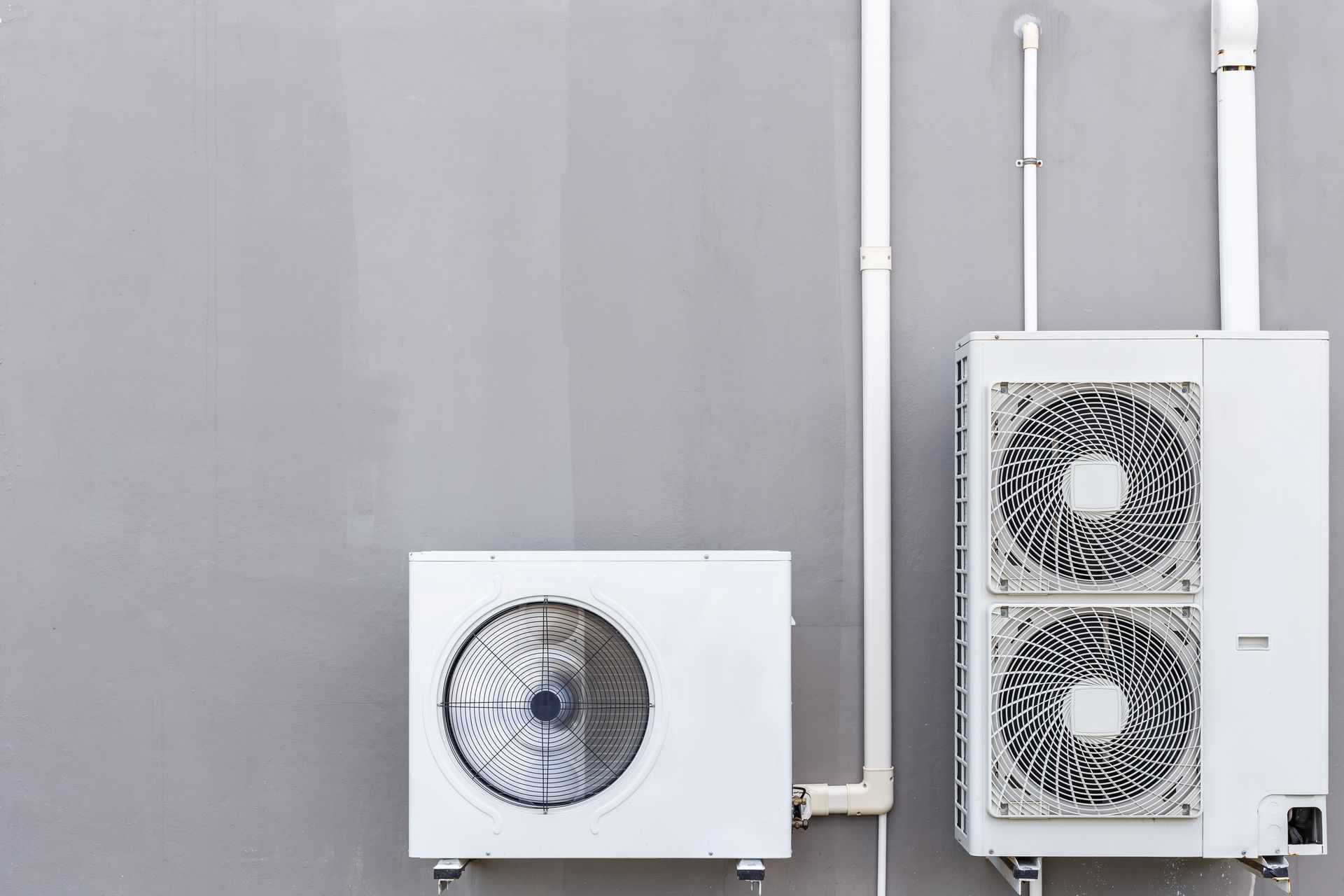 Unités de climatisation extérieures et tuyauterie montées sur un mur gris clair