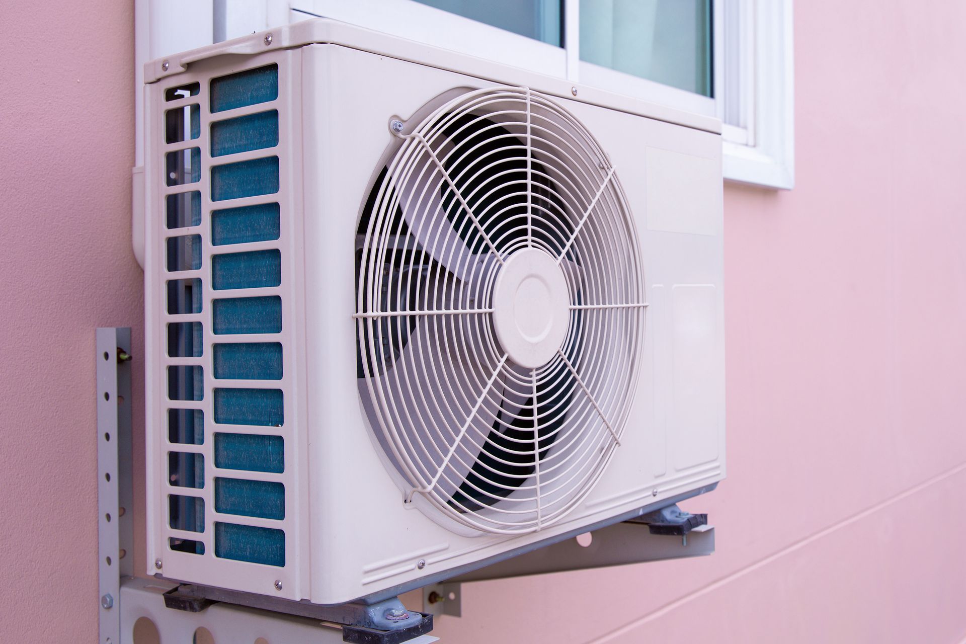 Unité de climatisation extérieure fixée sur un mur rose à côté d'une fenêtre