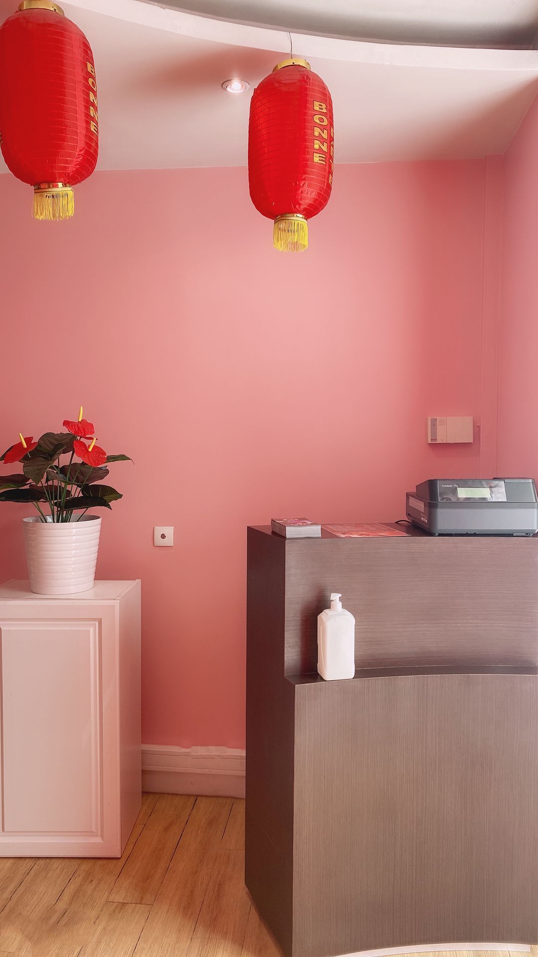 Pièce rose avec des lanternes rouges, une plante en pot et un petit comptoir d'accueil.