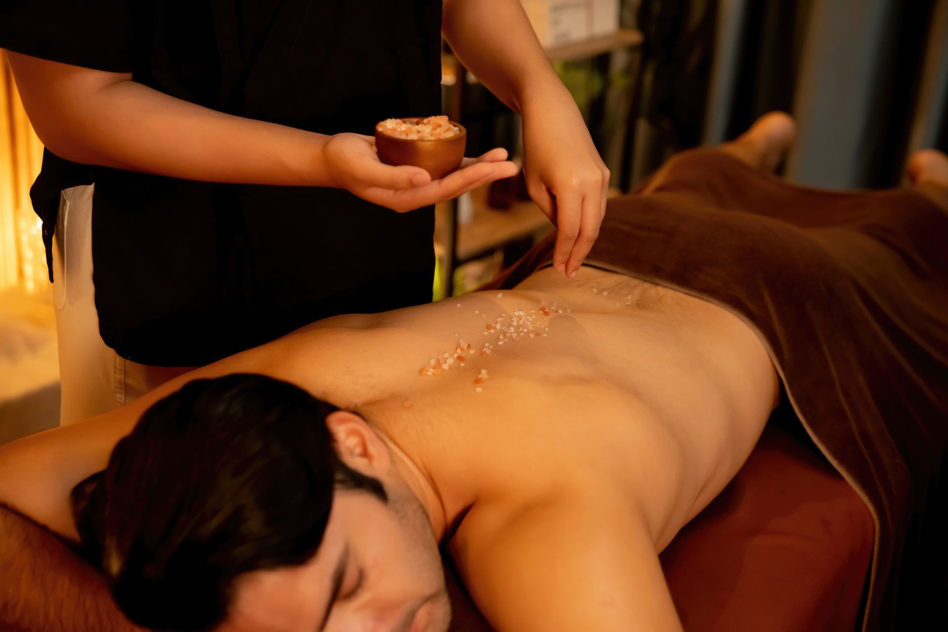 Massage spa sur une personne allongée sur le ventre, avec application d'huile sur le dos dans une lumière chaude.