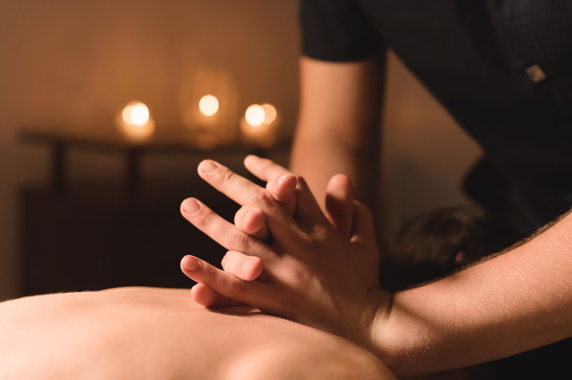 Des mains massent le dos d'une personne dans un spa à l'éclairage tamisé, éclairé aux bougies.