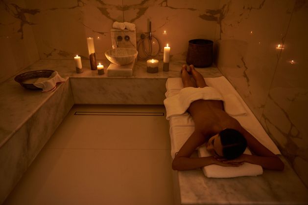 Une personne allongée sur une table de massage dans un spa, à la lueur des bougies, dans une pièce chaleureuse et tamisée.