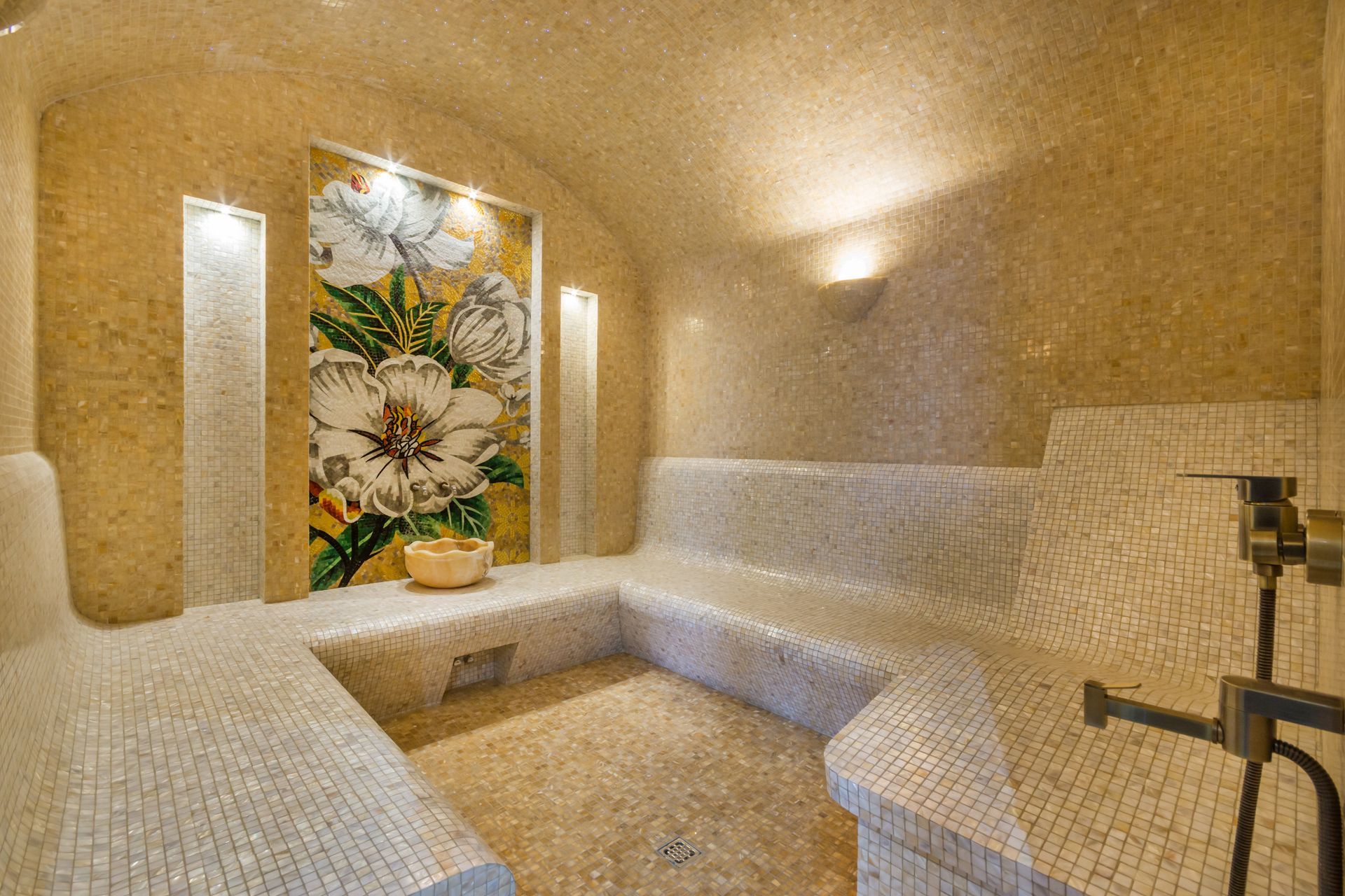 Petit espace spa avec banquettes blanches, éclairage tamisé et panneau mural fleuri.