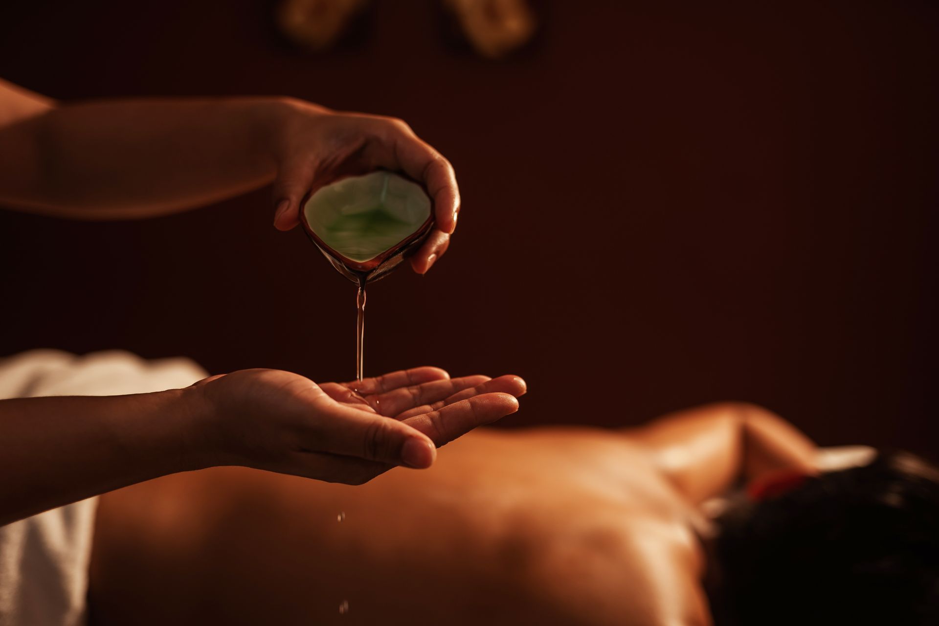Main versant de l'huile verte dans la paume ouverte lors d'un massage au spa.