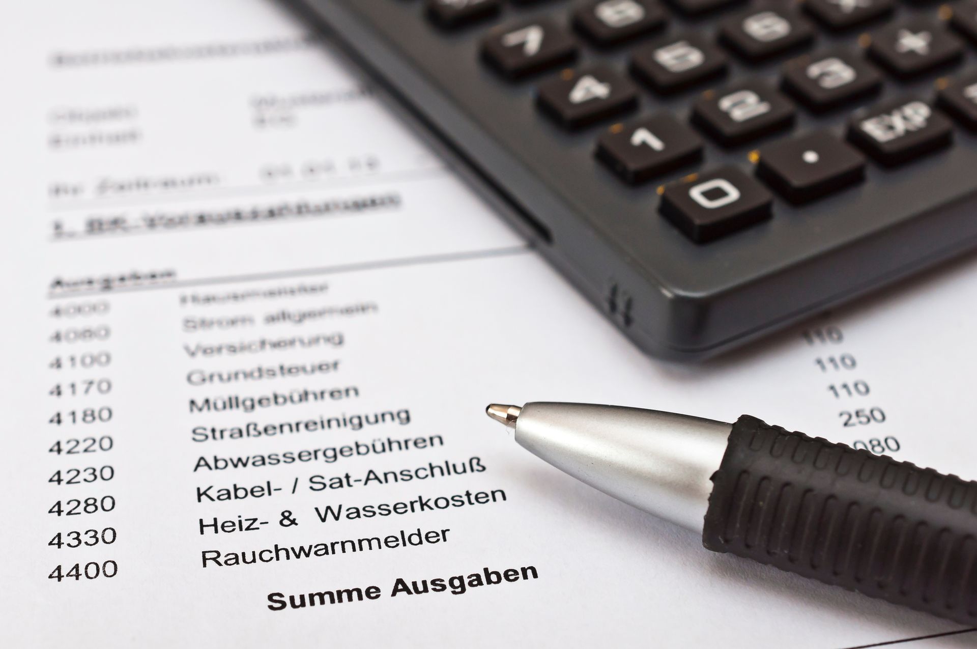 Ein Stift und ein Taschenrechner liegen auf einem Dokument, auf dem finanzielle Ausgaben aufgelistet