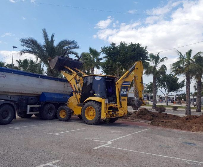 Una excavadora amarilla está cargando tierra en un camión volquete en un estacionamiento.