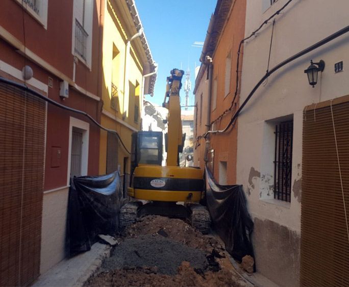 Una excavadora amarilla está trabajando en un callejón estrecho.