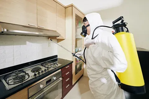 Un hombre con un traje de protección está rociando una cocina con un rociador.