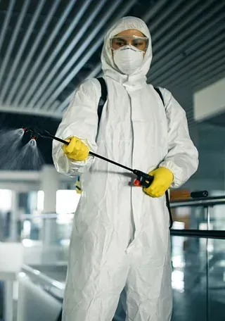 Un hombre con un traje de protección está rociando una habitación con un pulverizador.