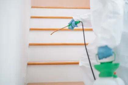 Un hombre con un traje de protección está rociando productos químicos en el suelo de una sala de estar.