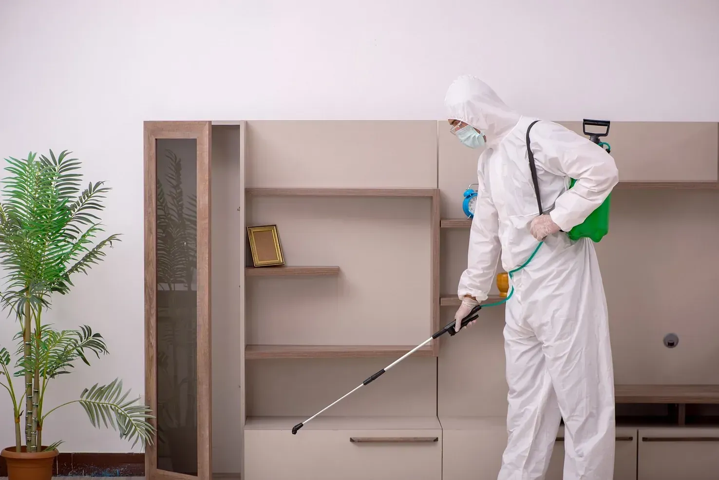 Un hombre con un traje de protección está rociando una habitación con un pulverizador.