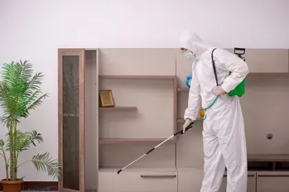 Un hombre con un traje de protección está rociando productos químicos en el suelo de una sala de estar.