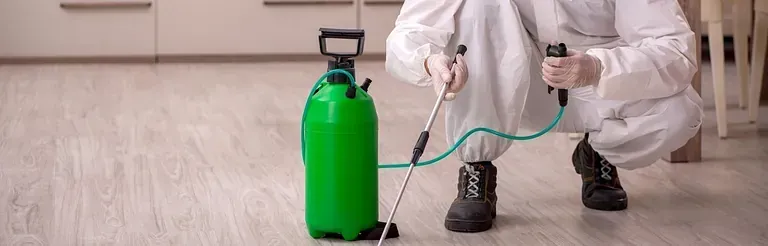 Un hombre con un traje de protección está rociando una botella verde con un pulverizador.