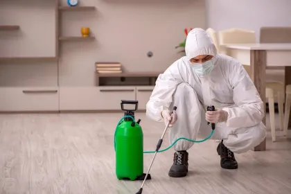 Un hombre con un traje de protección está rociando productos químicos en el suelo de una sala de estar.