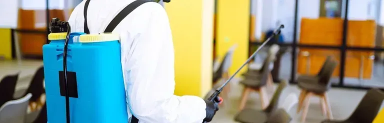 Un hombre con un traje de protección está rociando una habitación con un pulverizador.