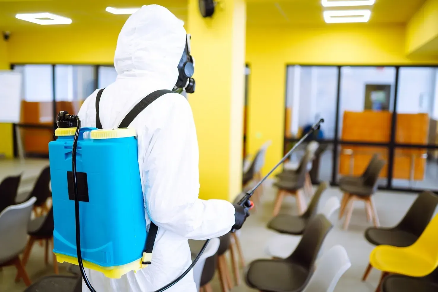 Un hombre con un traje de protección está desinfectando una habitación con un pulverizador.