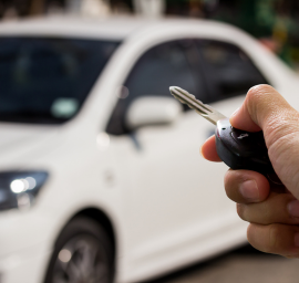 Une personne tient une clé de voiture devant une voiture blanche