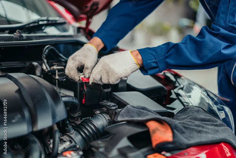 Un mécanicien en combinaison bleue et gants travaille sur un moteur de voiture.