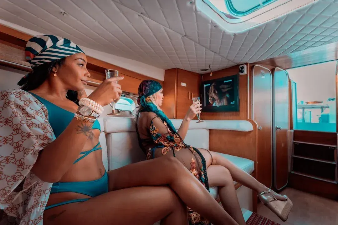 Barco a motor blanco en un puerto, con edificios en la ladera al fondo bajo un cielo azul.