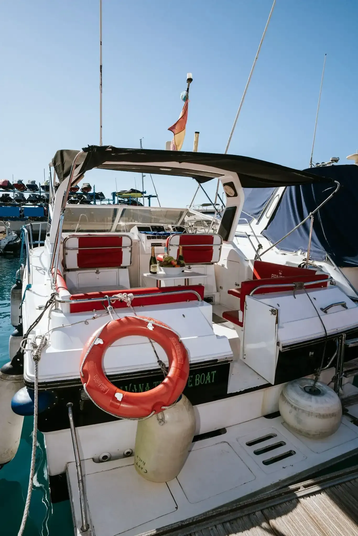 Velero en el agua al atardecer. Casco blanco, velas azules, toldo negro. Aguas tranquilas, luz dorada.