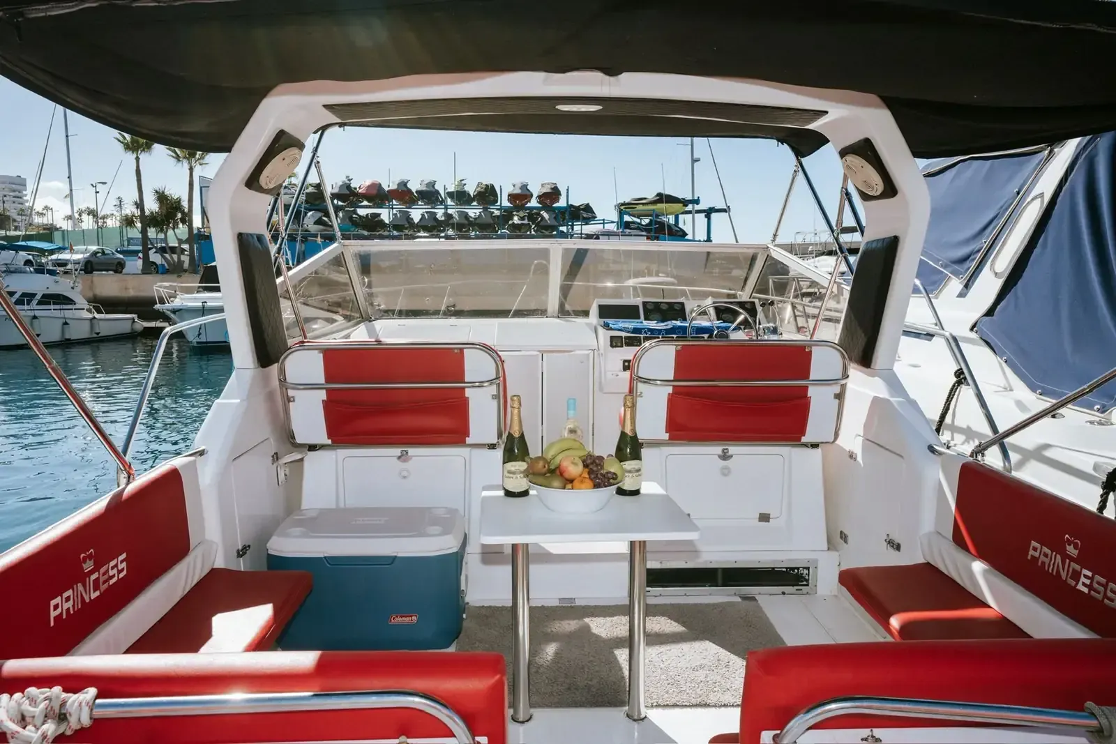 Interior de barco Princess rojo y blanco con champán y mesa, hielera azul y vista al mar.
