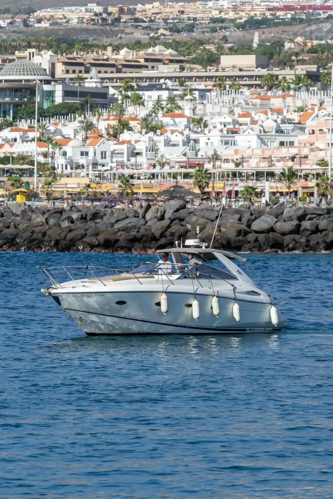 Lancha motora blanca sobre agua azul, fondo de ciudad costera.