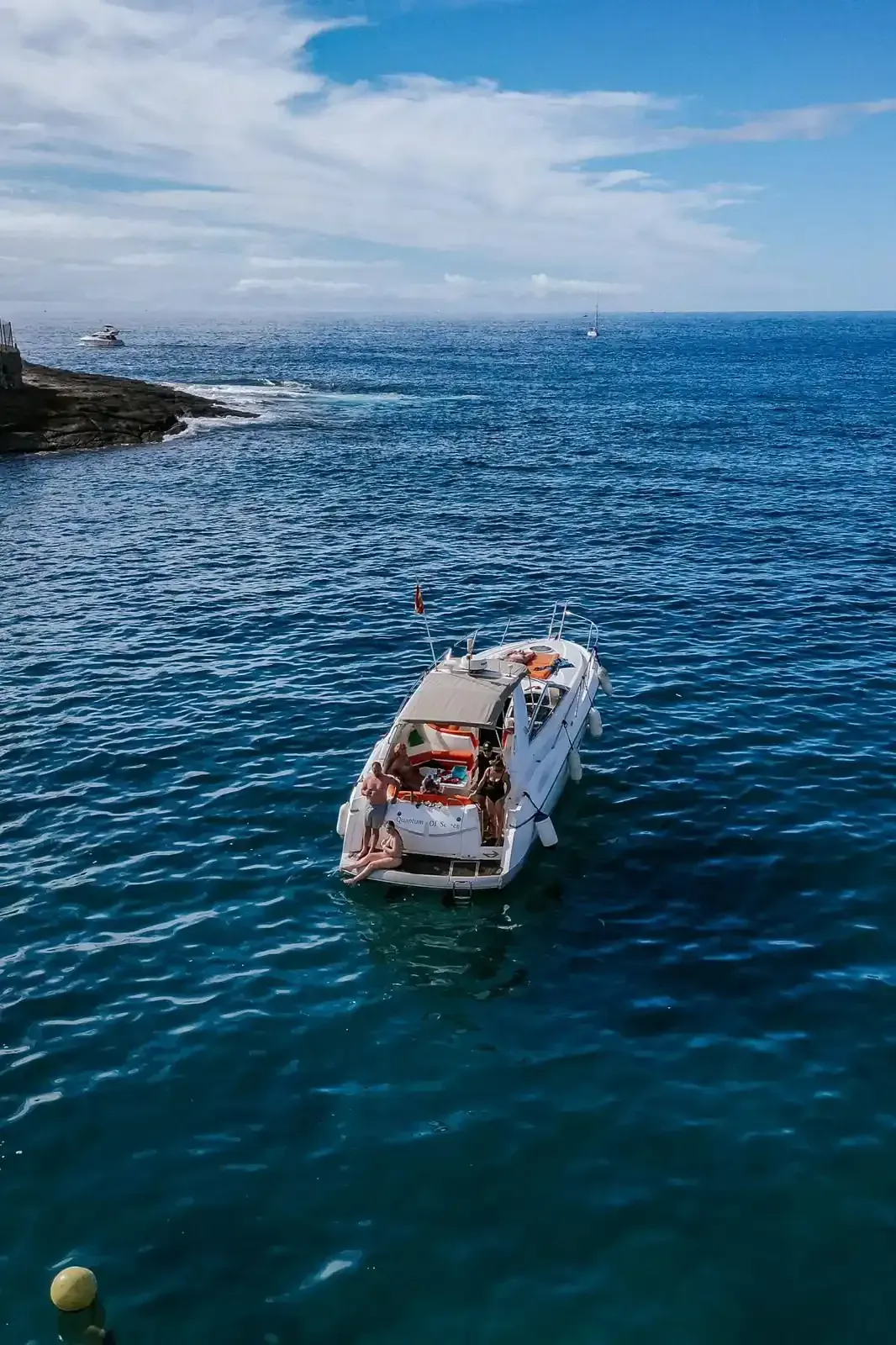 Barco a motor blanco en un puerto, con edificios en la ladera al fondo bajo un cielo azul.