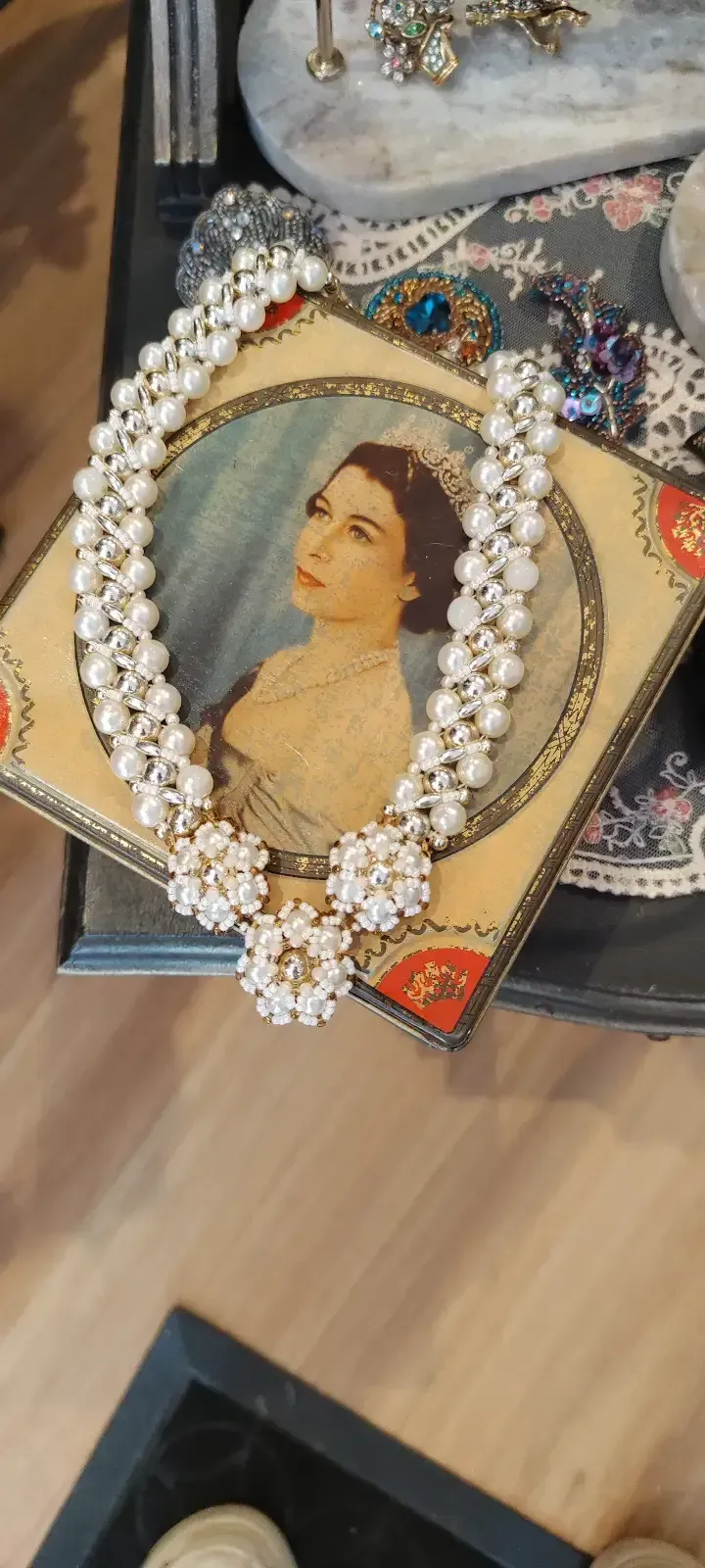 Un collar de perlas cubre un retrato sobre una mesa, con otras joyas al fondo.