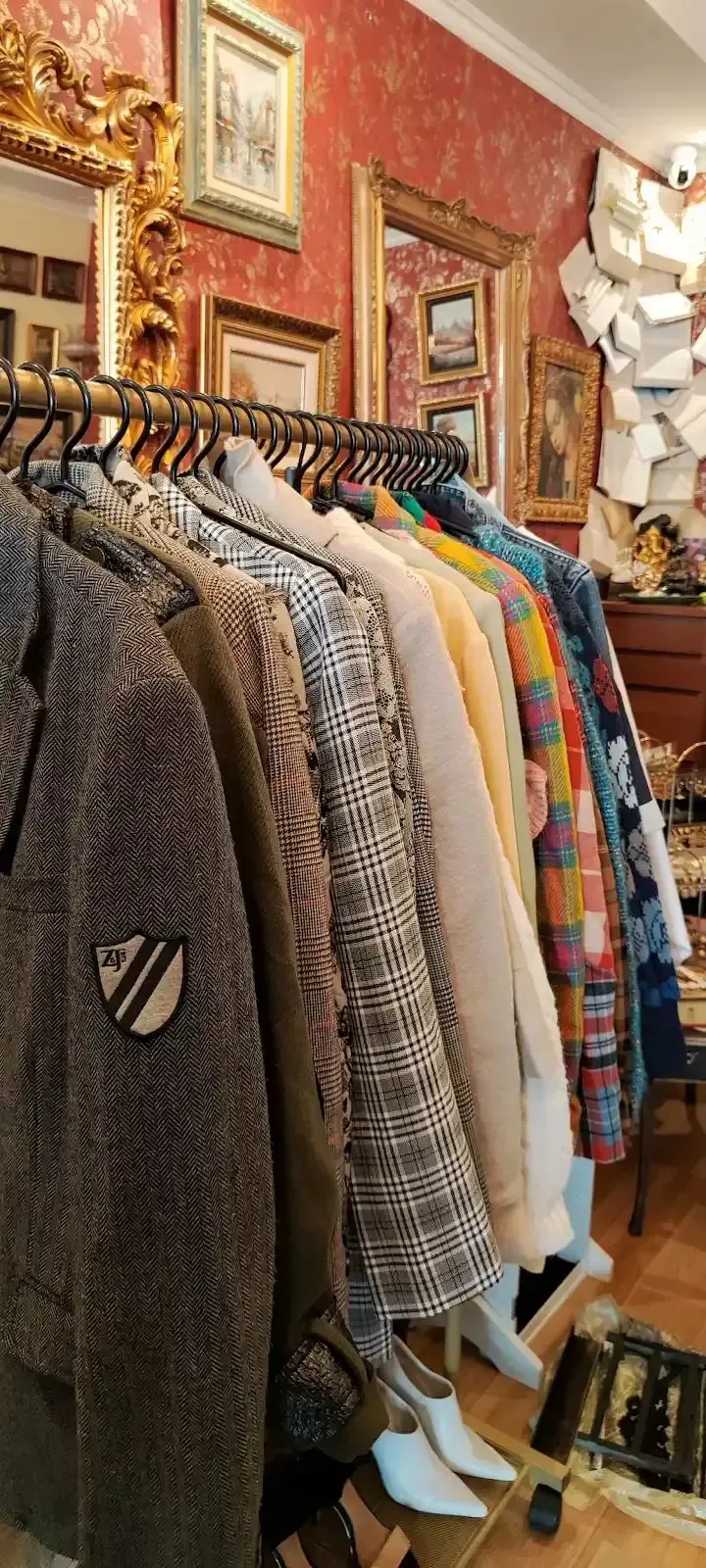 Un perchero con chaquetas vintage en una habitación con espejos dorados ornamentados y papel pintado rojo.