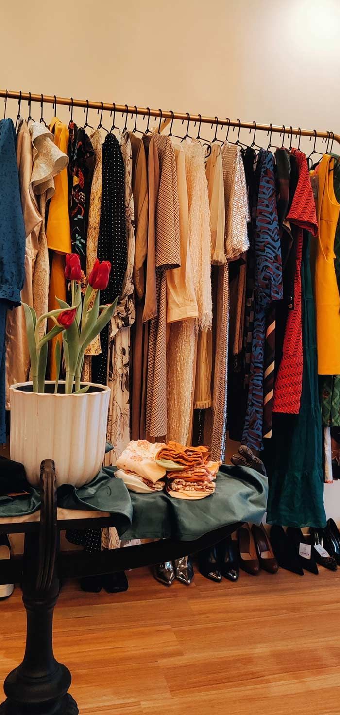 Perchero con vestidos, flores en macetas y suelo de madera.