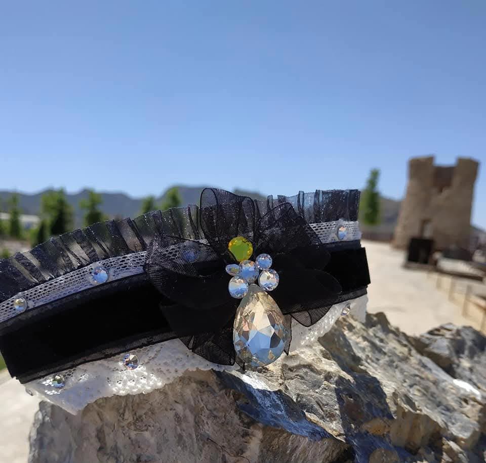 Liga blanca y negra decorada con joyas sobre muro de piedra, torre y montañas al fondo.