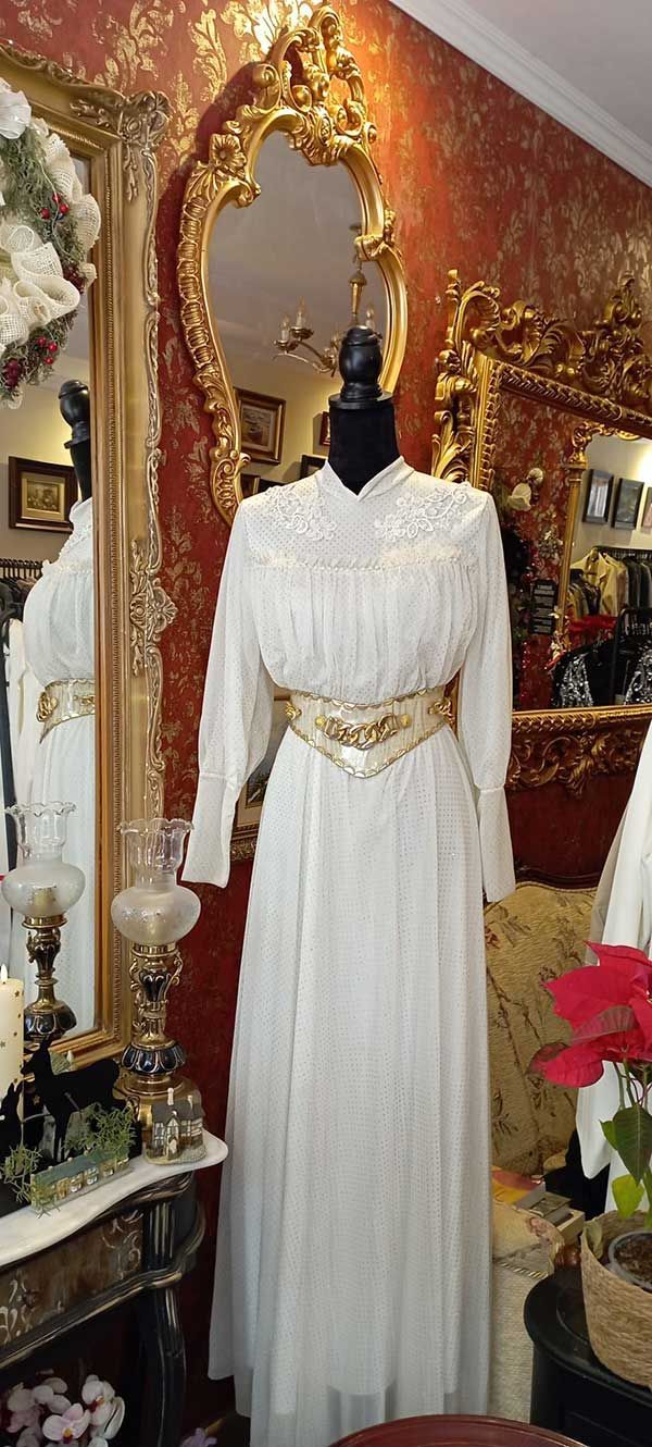 Vestido blanco sobre maniquí con cinturón dorado, expuesto en tienda vintage.