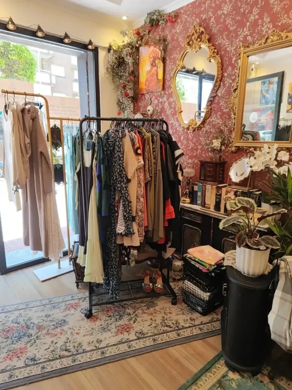 Interior de una tienda de ropa con percheros, papel pintado floral, espejos y alfombras.