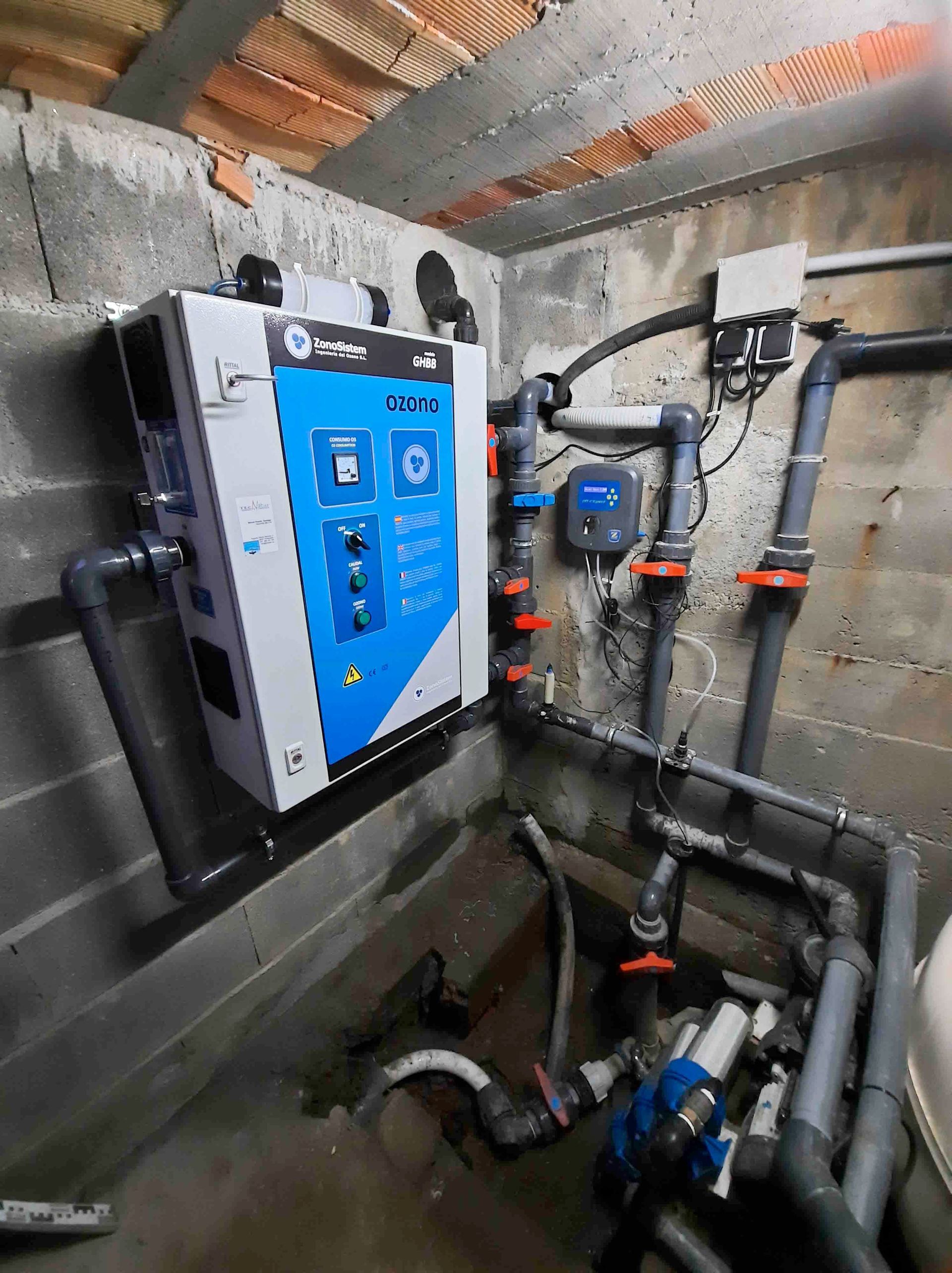 Sala de calderas con una unidad azul montada en la pared, tuberías, válvulas y paredes de hormigón en un espacio de servicio