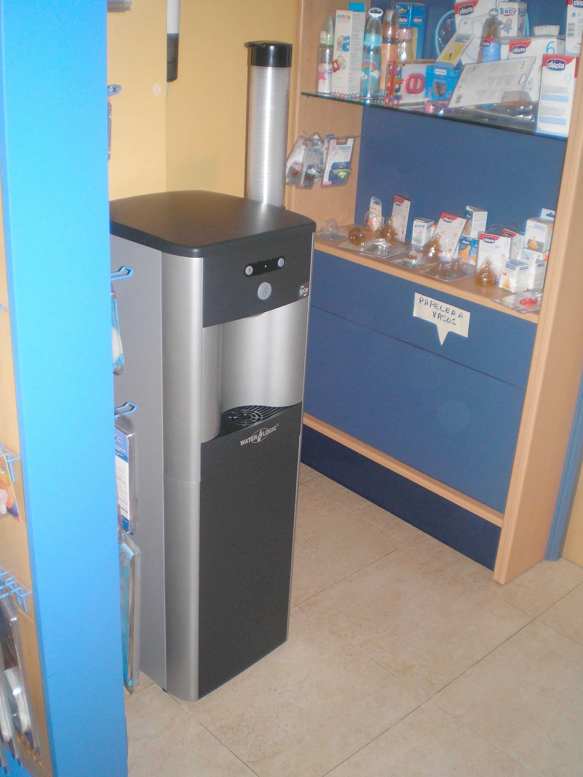 Fuente de agua de acero inoxidable de pie junto a una estantería azul y de madera en una tienda.