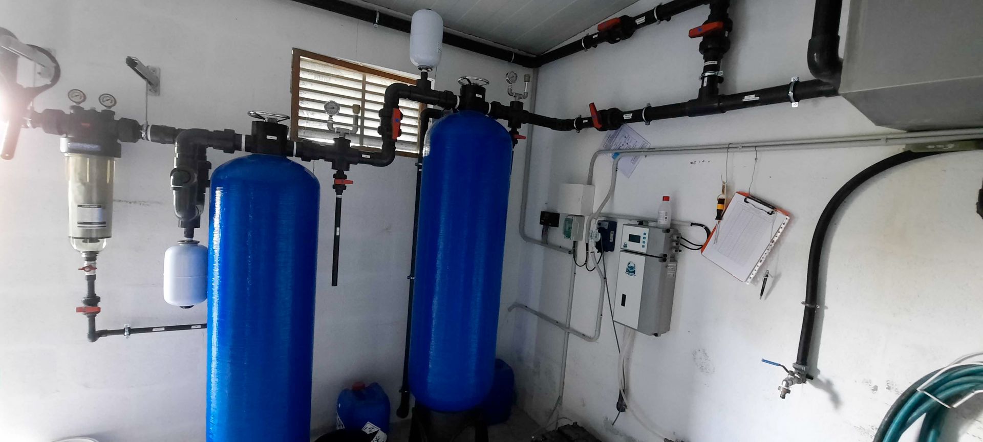 Sistema de filtración de agua interior con dos tanques azules y tuberías en una pared blanca