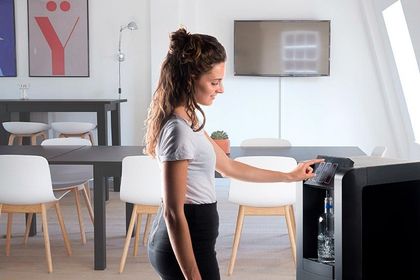 Mujer de pie junto a un escritorio en una oficina luminosa, usando una cafetera
