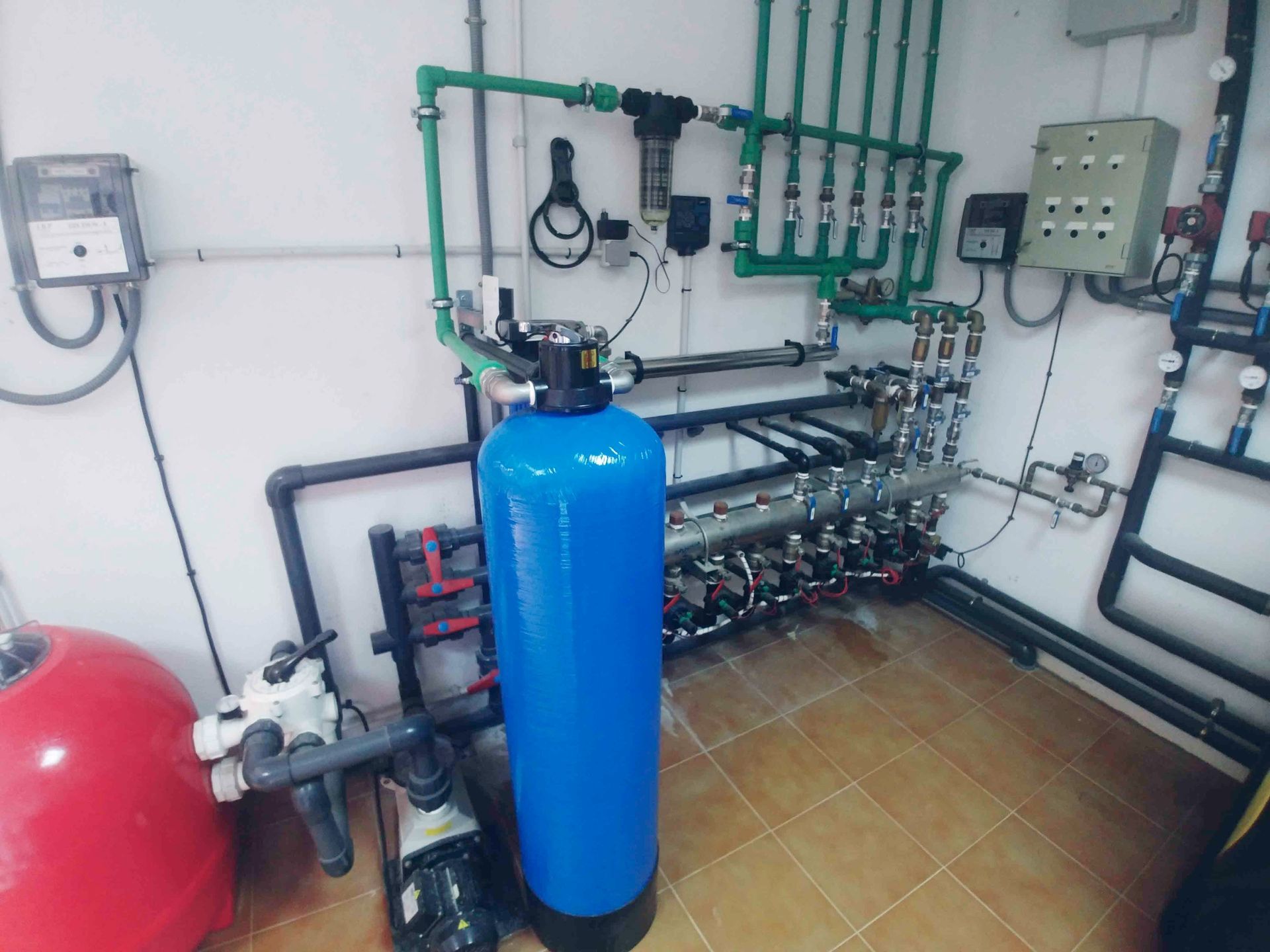 Sala de tratamiento industrial de agua con tanque azul, depósito a presión rojo, tuberías, válvulas y paneles de control
