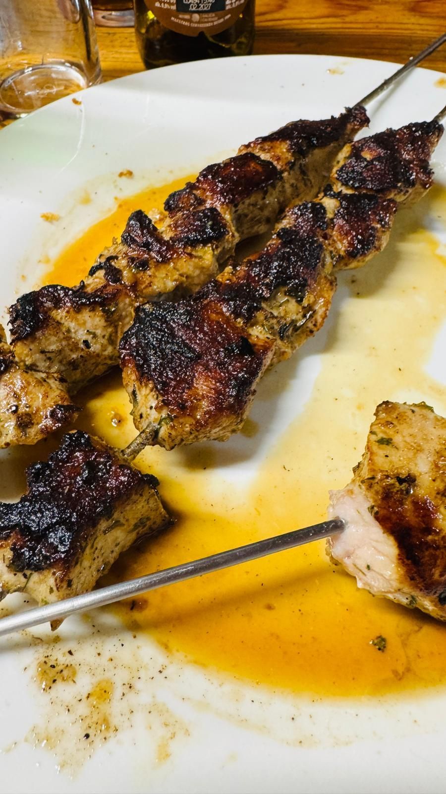 Brochetas de carne a la parrilla en un plato blanco con salsa de naranja y un trozo en un pincho de metal.
