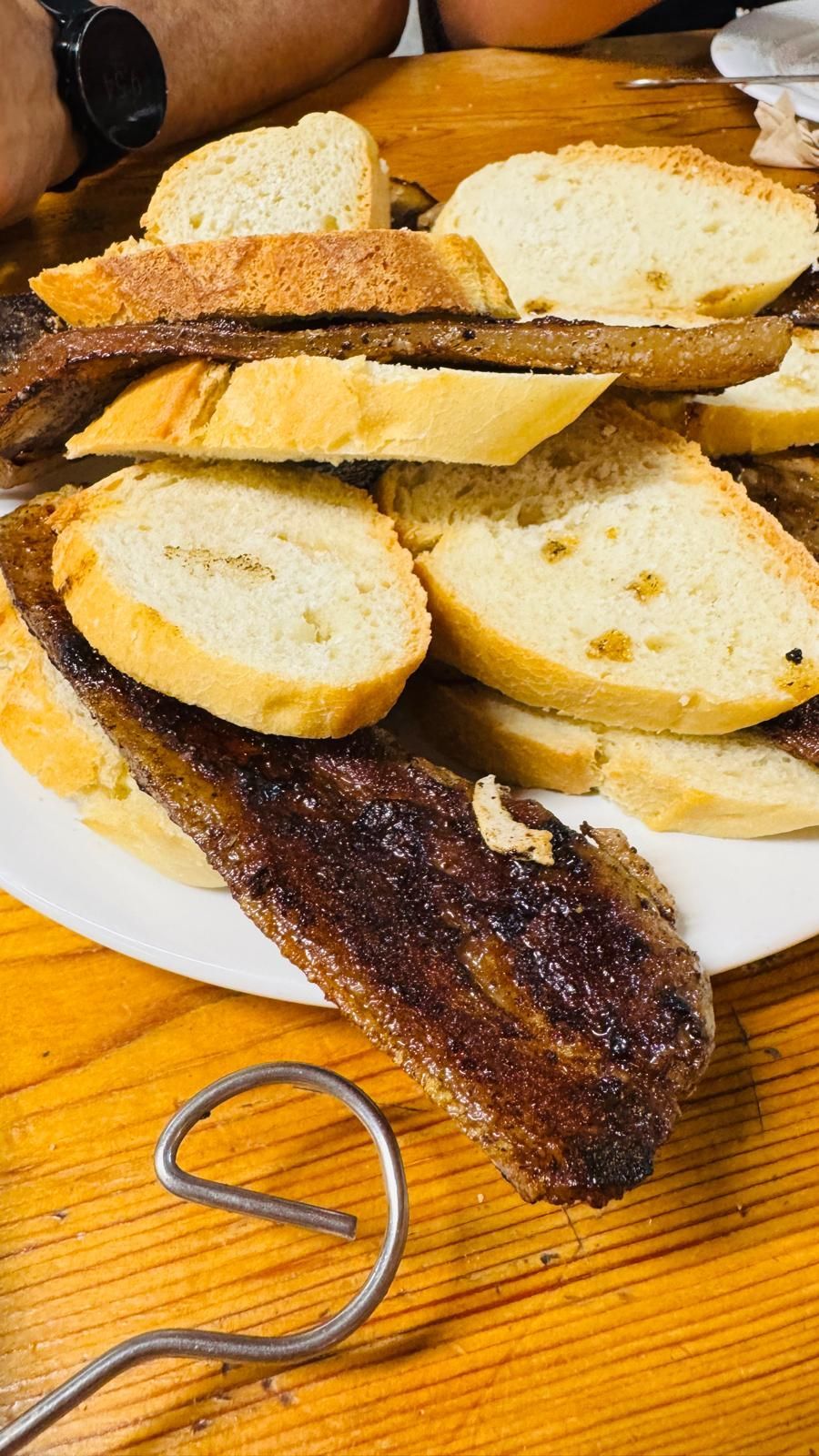 Plato de pan rebanado sobre una mesa de madera, con un utensilio de mango de madera oscura cerca.