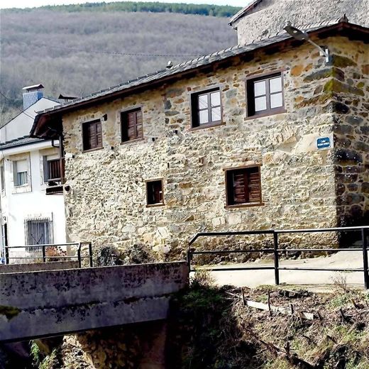 Casa de piedra con contraventanas marrones junto a un pequeño puente en un pueblo rural en la ladera de una colina.