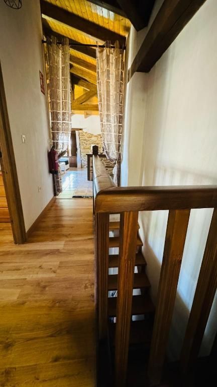 Pasillo de madera con vigas y barandilla a la vista que da a una escalera interior rústica.