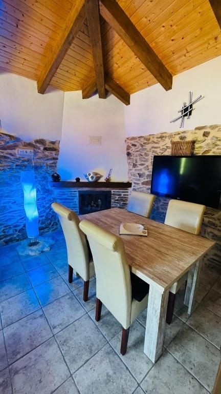 Acogedor comedor rústico con techo abovedado de madera, paredes de piedra, mesa, sillas, televisor e iluminación ambiental azul.