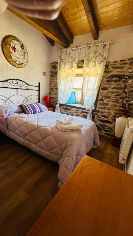 Habitación acogedora con cama de metal, techo de madera, pared de piedra y luz natural que se filtra a través de cortinas de encaje.