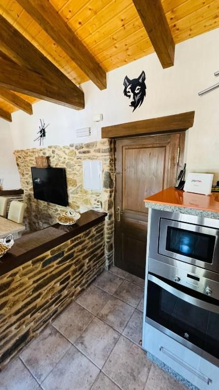 Rincón de cocina rústica con vigas de madera, encimera de piedra, suelo de baldosas y horno empotrado junto a una puerta de madera.