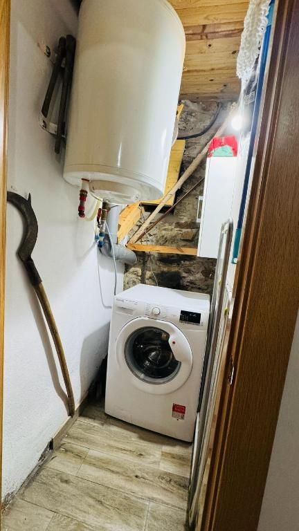 Armario estrecho para herramientas que contiene un calentador de agua, una lavadora y utensilios de limpieza.
