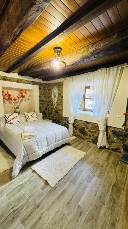 Acogedora habitación con ropa de cama blanca, techo con vigas de madera, pared de piedra y ventana con cortinas.
